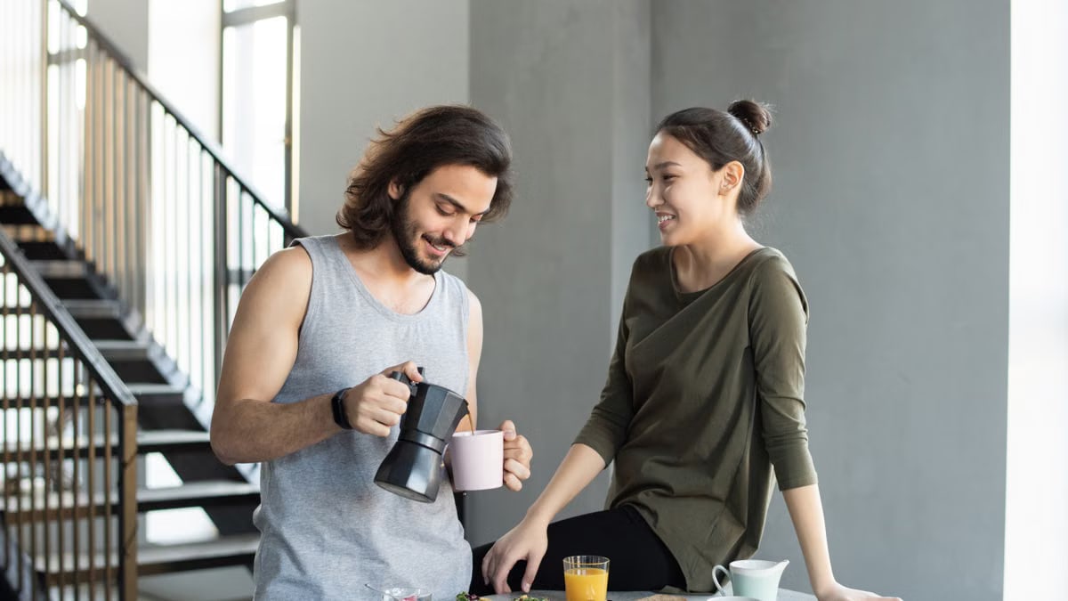 A couple enjoy a casual breakfast indoors with coffee and food, smiling and relaxed.